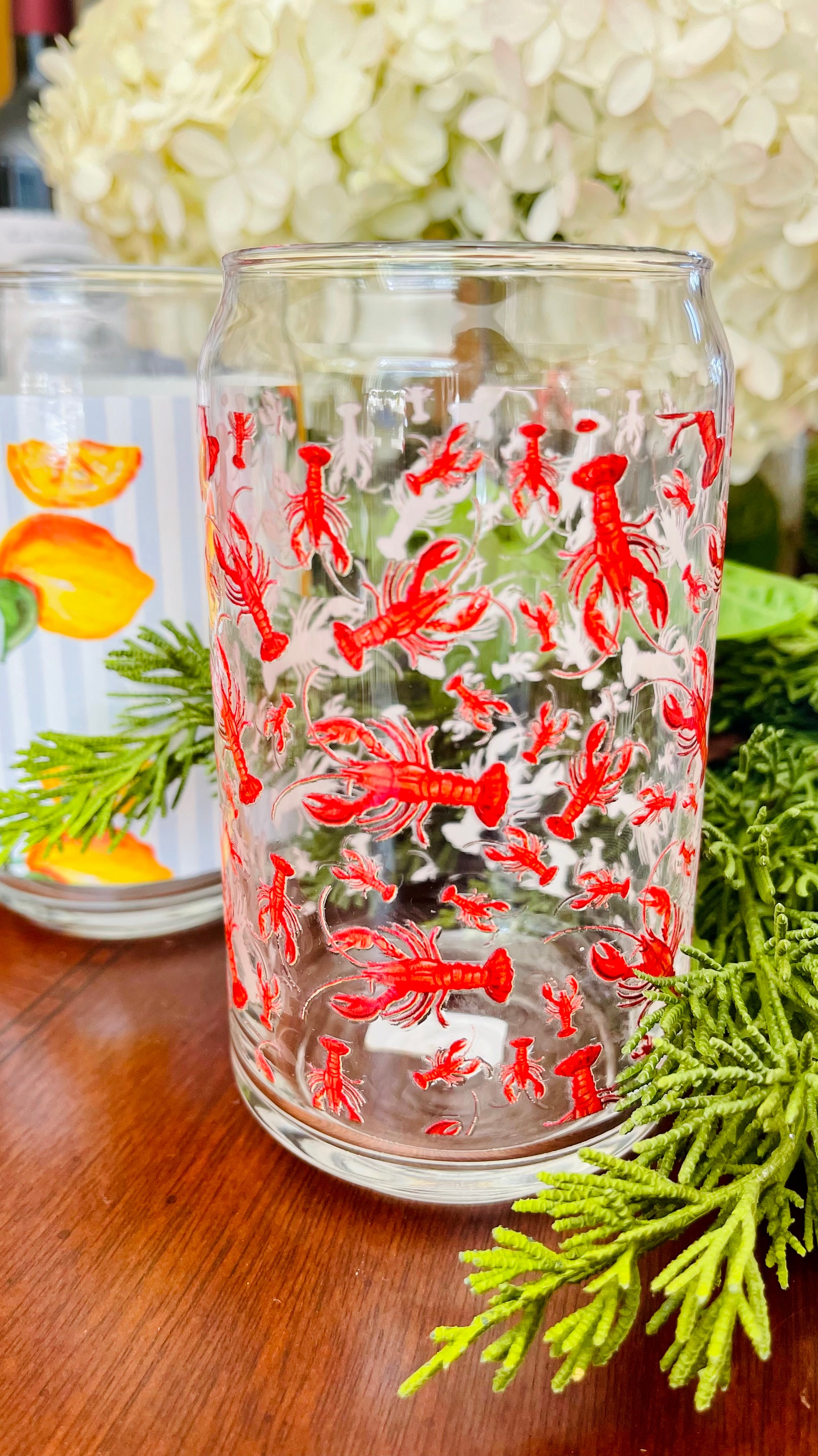Clear glass with red lobster design on a wooden surface with greenery