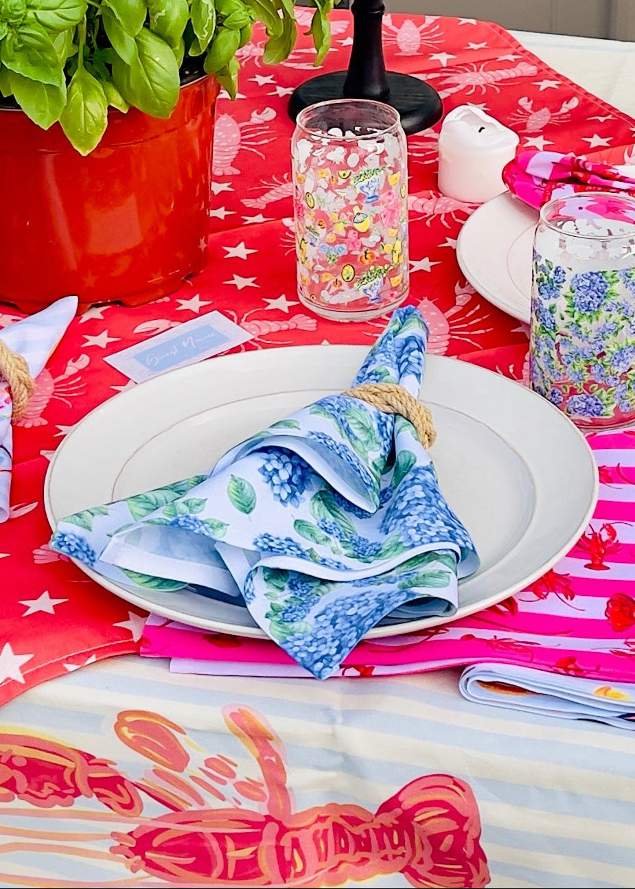 Decorated table with a red and white tablecloth, colorful napkins, and various items on a patio.