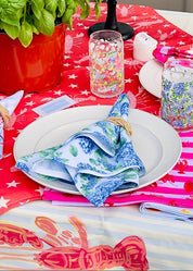 Decorated table with a red and white tablecloth, colorful napkins, and various items on a patio.