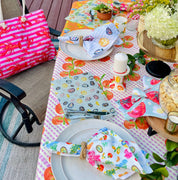Outdoor table setting with colorful tablecloth, plates, and napkins on a deck.