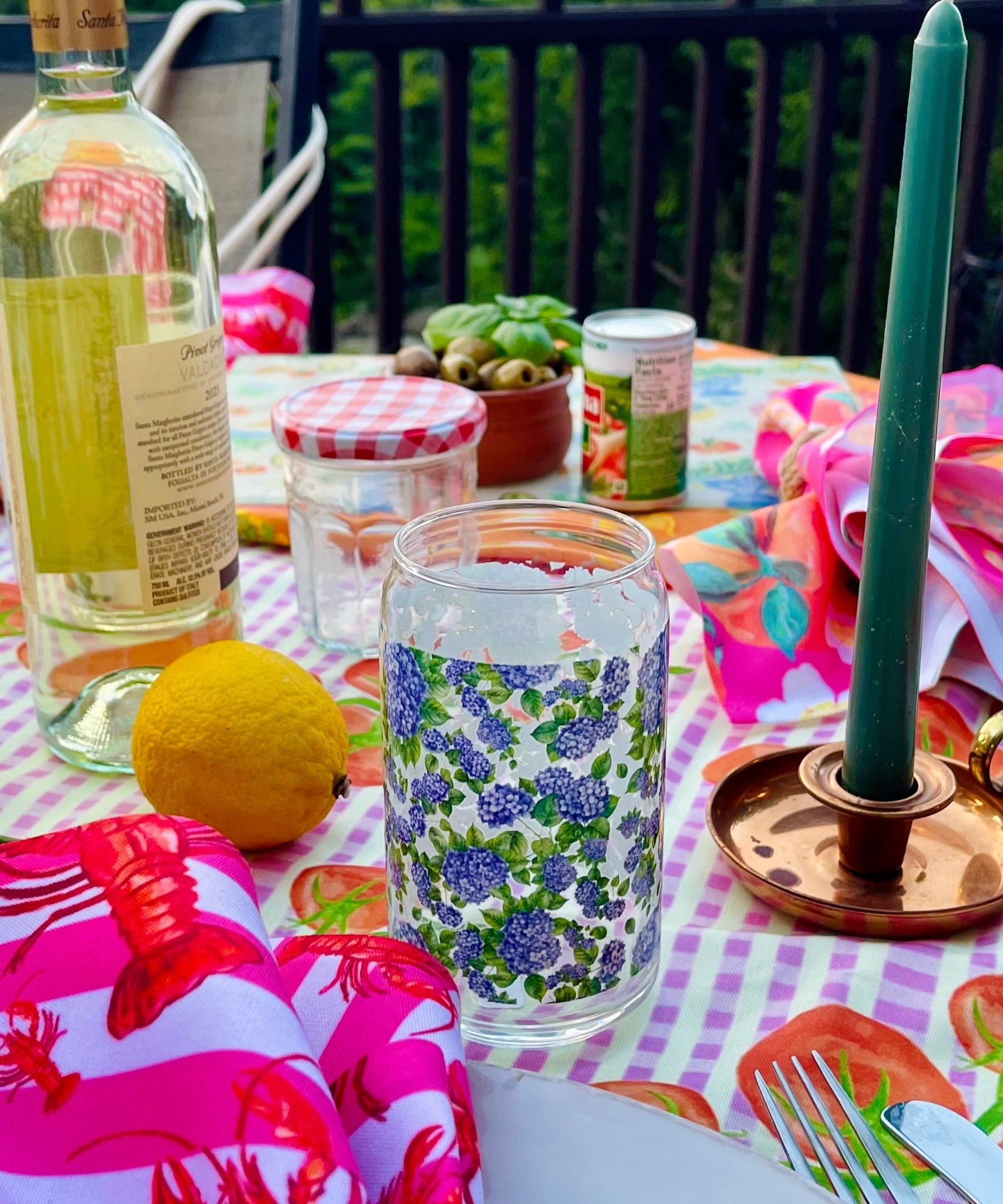 Outdoor table setting with colorful tablecloth, wine bottle, and decorative items on a deck.