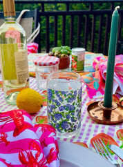 Outdoor table setting with colorful tablecloth, wine bottle, and decorative items on a deck.