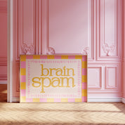 Brain Spam horizontal 24x36 mental health wall art poster leaning against a pink paneled wall on a herringbone wood floor