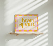 Brain Spam horizontal 24x36 mental health wall art poster displayed on a wooden shelf against a sunlit white wall