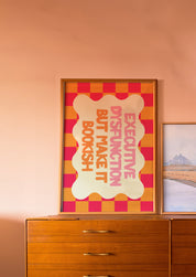 Executive Dysfunction but Make It Bookish 24x36 bookish mental health wall art poster leaning on a wooden dresser against a blush wall