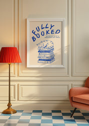 Fully Booked 24x36 bookish wall art poster framed on a cream paneled wall beside a red lamp