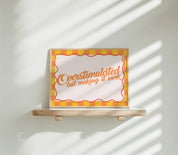Overstimulated but Making It Work horizontal 24x36 mental health wall art poster displayed on a wooden shelf against a sunlit white wall