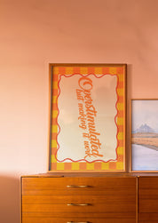 Overstimulated but Making It Work 24x36 mental health wall art poster leaning on a wooden dresser against a blush wall