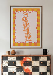 Overstimulated but Making It Work 24x36 mental health wall art poster framed above a black and white checkered dresser