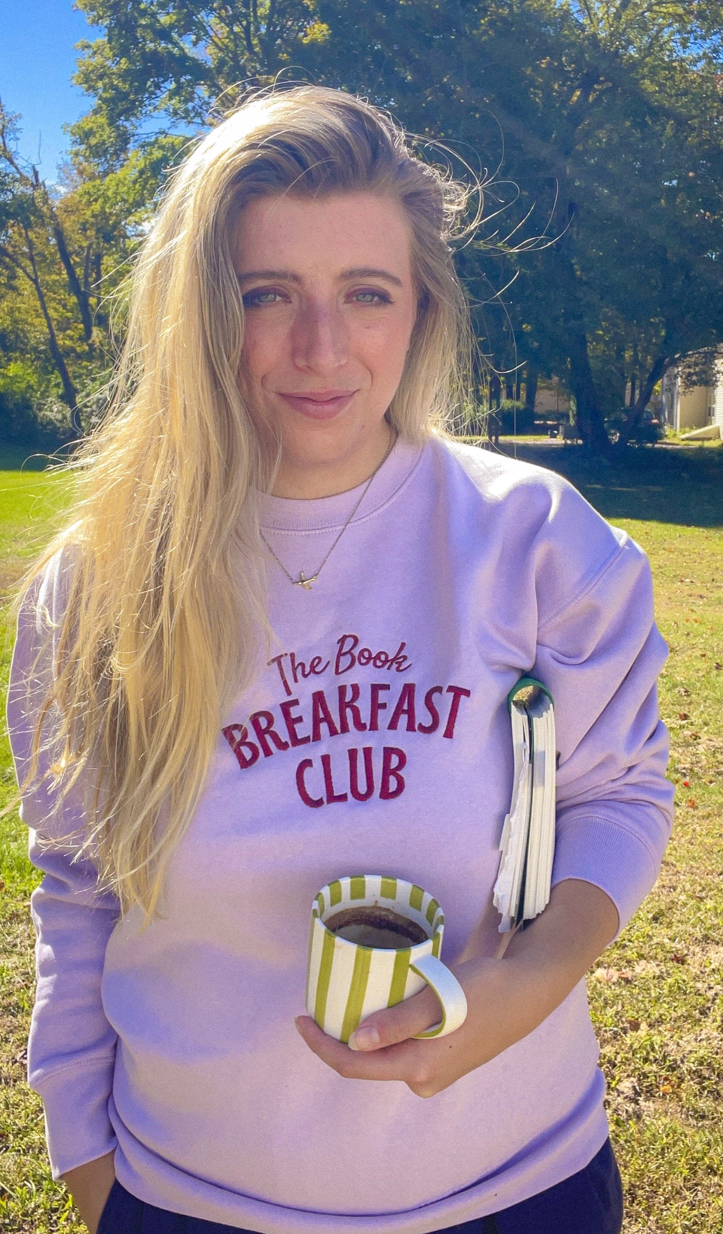 Woman wearing the lavender Book Breakfast Club embroidered sweatshirt holding a mug and book