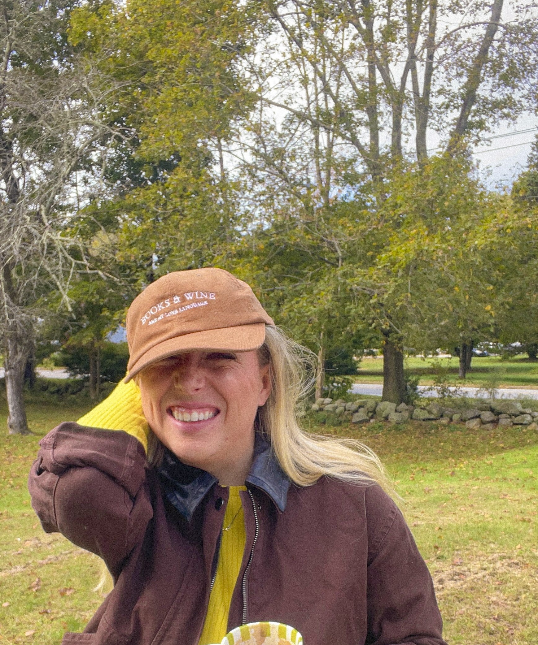 Woman wearing the brown Books & Wine embroidered corduroy hat with a mug outdoors