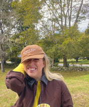 Woman wearing the brown Books & Wine embroidered corduroy hat with a mug outdoors
