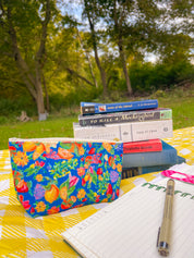 Citrus Garden in Blue accessory pouch with a stack of classic books on a picnic blanket