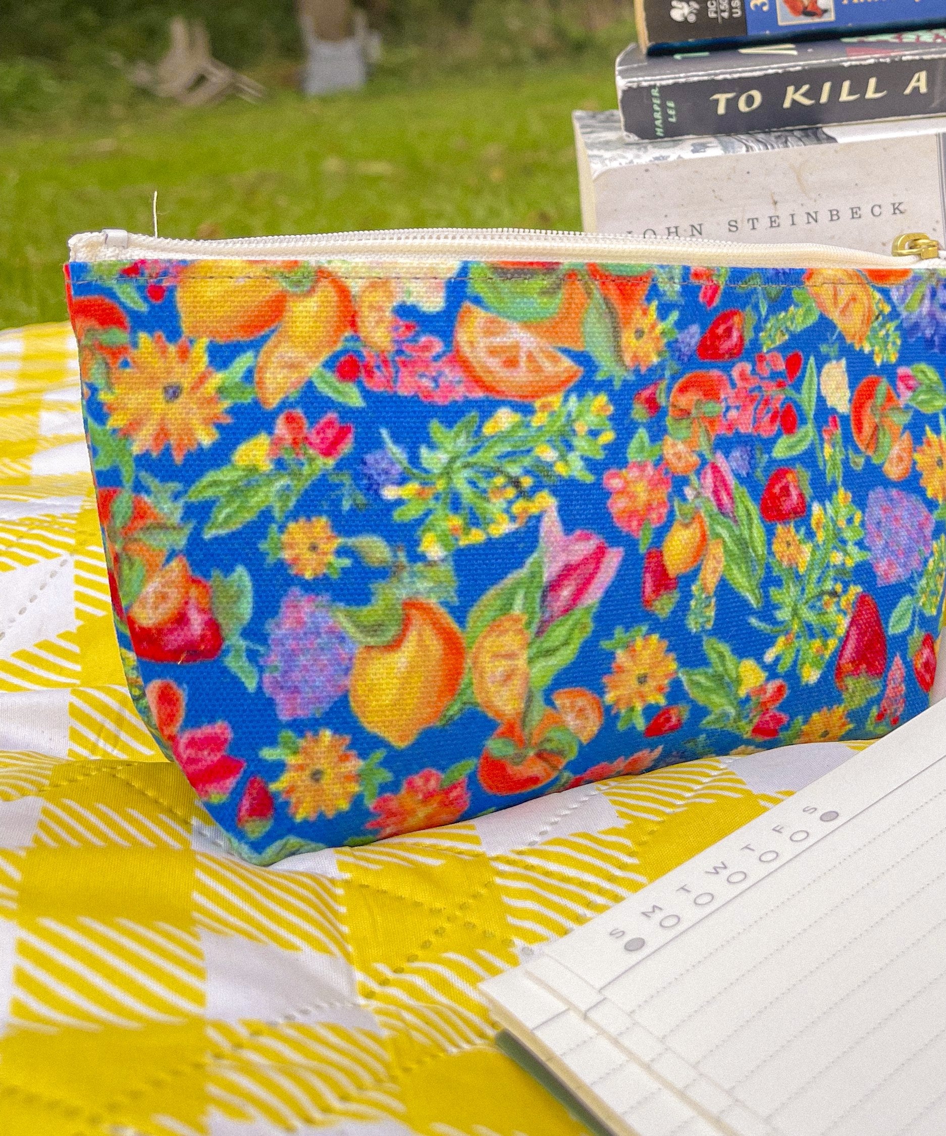Citrus Garden in Blue accessory pouch with a stack of classic books on a picnic blanket