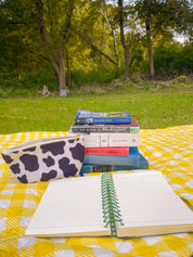 Cow print accessory pouch with books and a notebook on a yellow gingham blanket