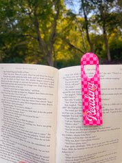 Pink Reading metal bookmark marking a page outdoors