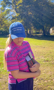 Woman wearing the Reading Is Cheaper Than Therapy embroidered denim hat holding a book