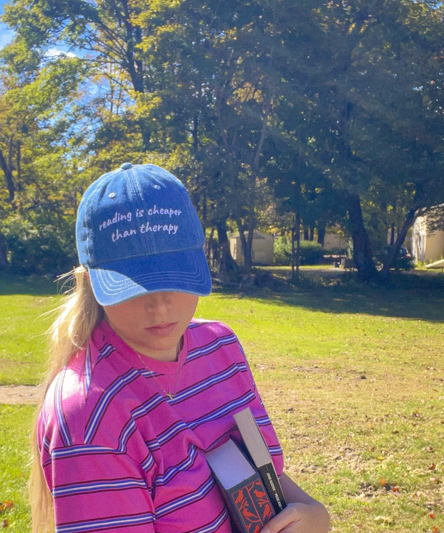 Woman wearing the Reading Is Cheaper Than Therapy embroidered denim hat holding a book