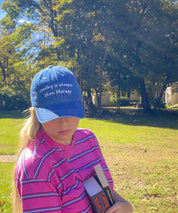 Woman wearing the Reading Is Cheaper Than Therapy embroidered denim hat holding a book