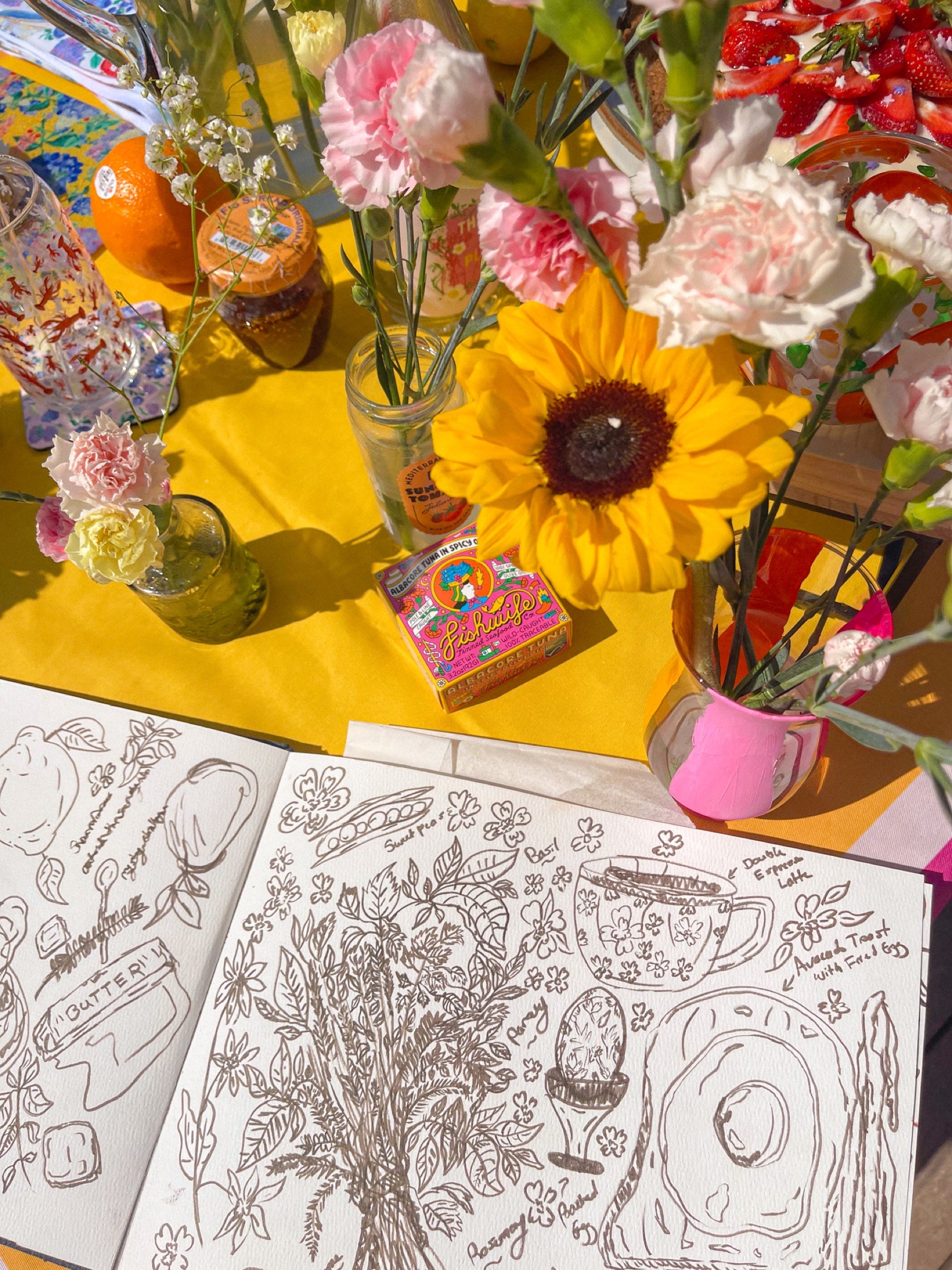 Open sketchbook of Sarah's original pen drawings on a sunny table with sunflowers