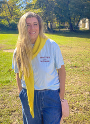 Woman wearing the Written by a Woman embroidered heavyweight tee with jeans and a yellow scarf