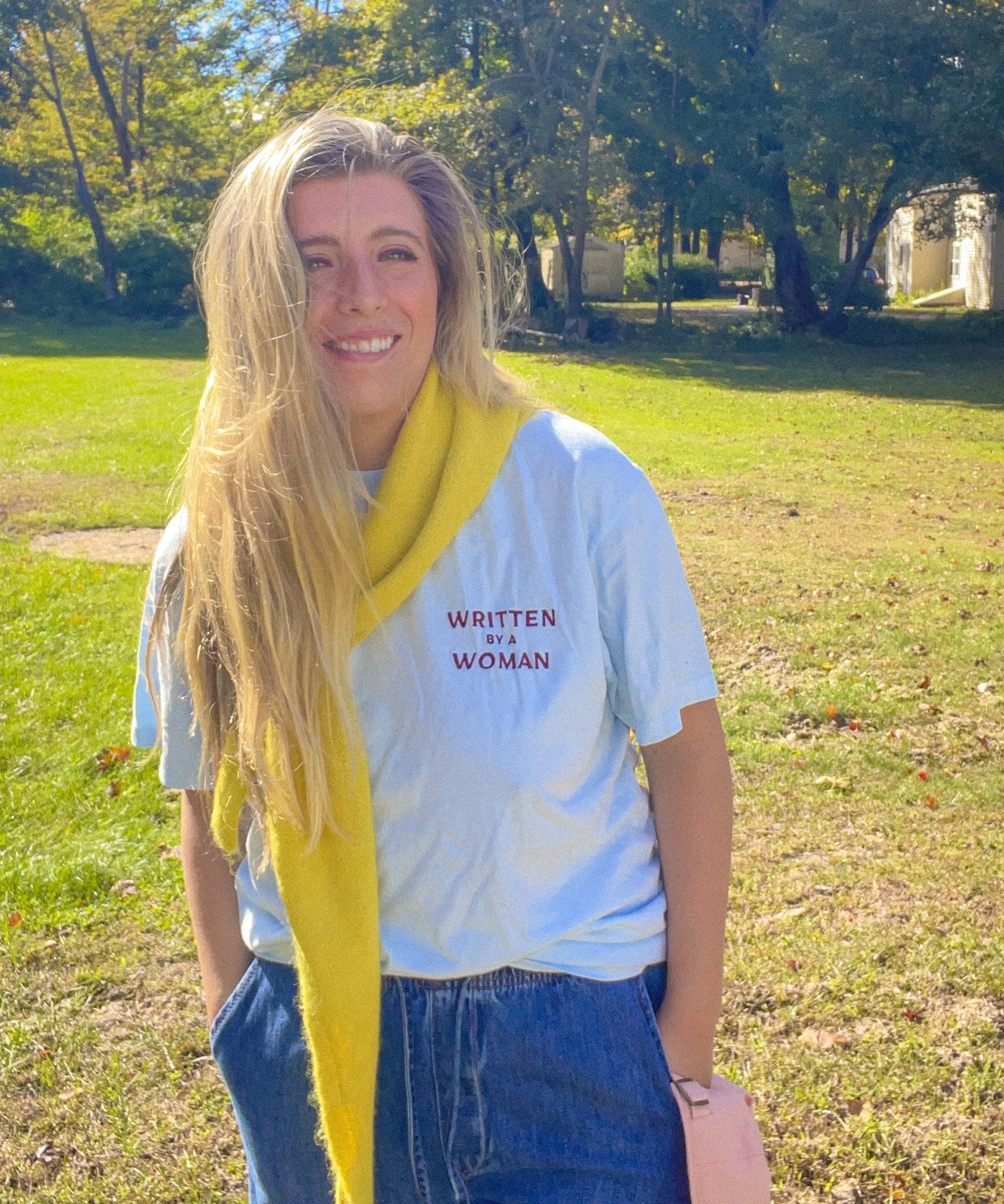 Woman wearing the Written by a Woman embroidered heavyweight tee with jeans and a yellow scarf