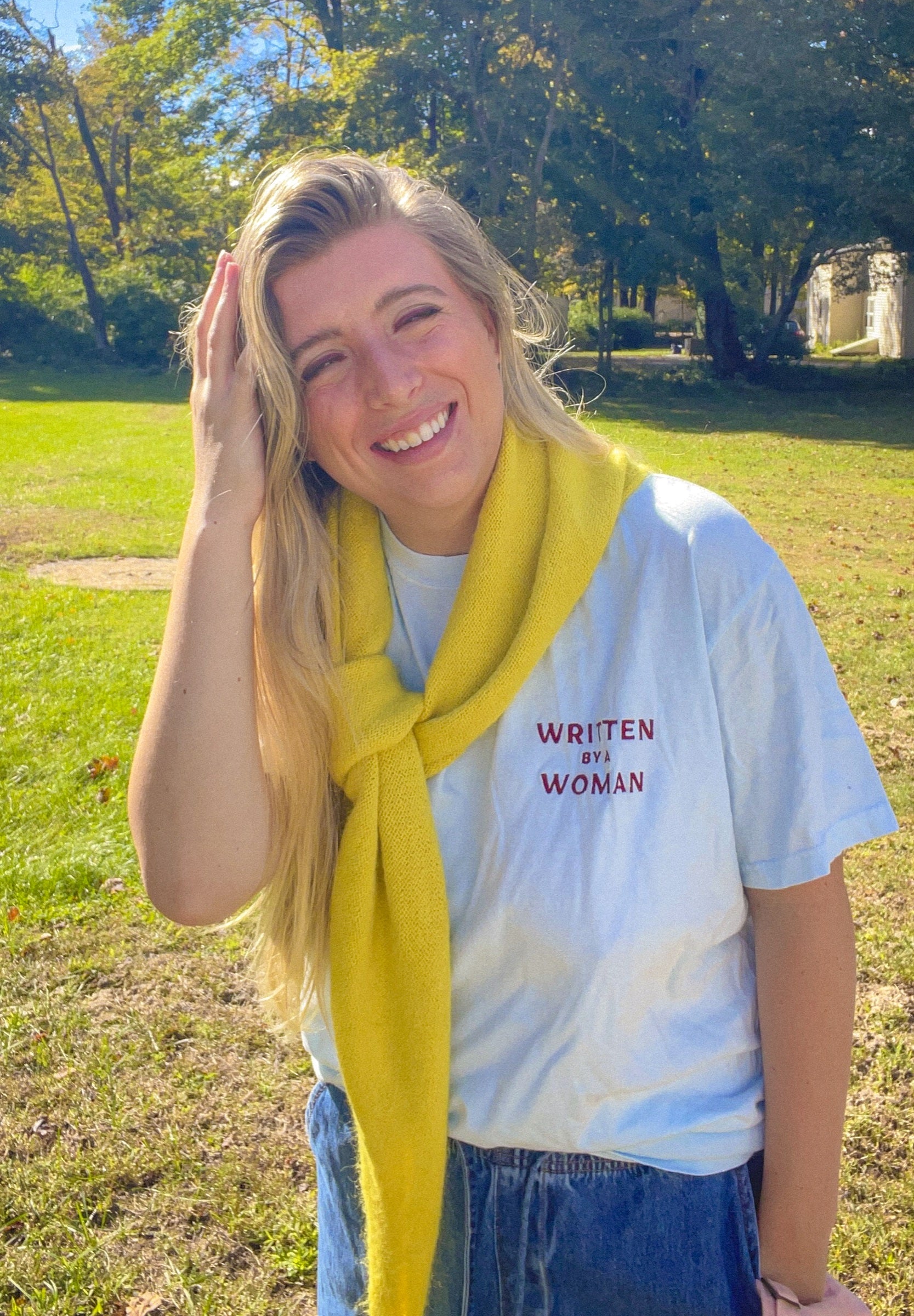 Sarah smiling in a Written by a Woman embroidered tee with a yellow scarf