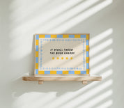 It Gives: Throw the Book Energy horizontal 24x36 bookish wall art poster displayed on a wooden shelf against a sunlit white wall