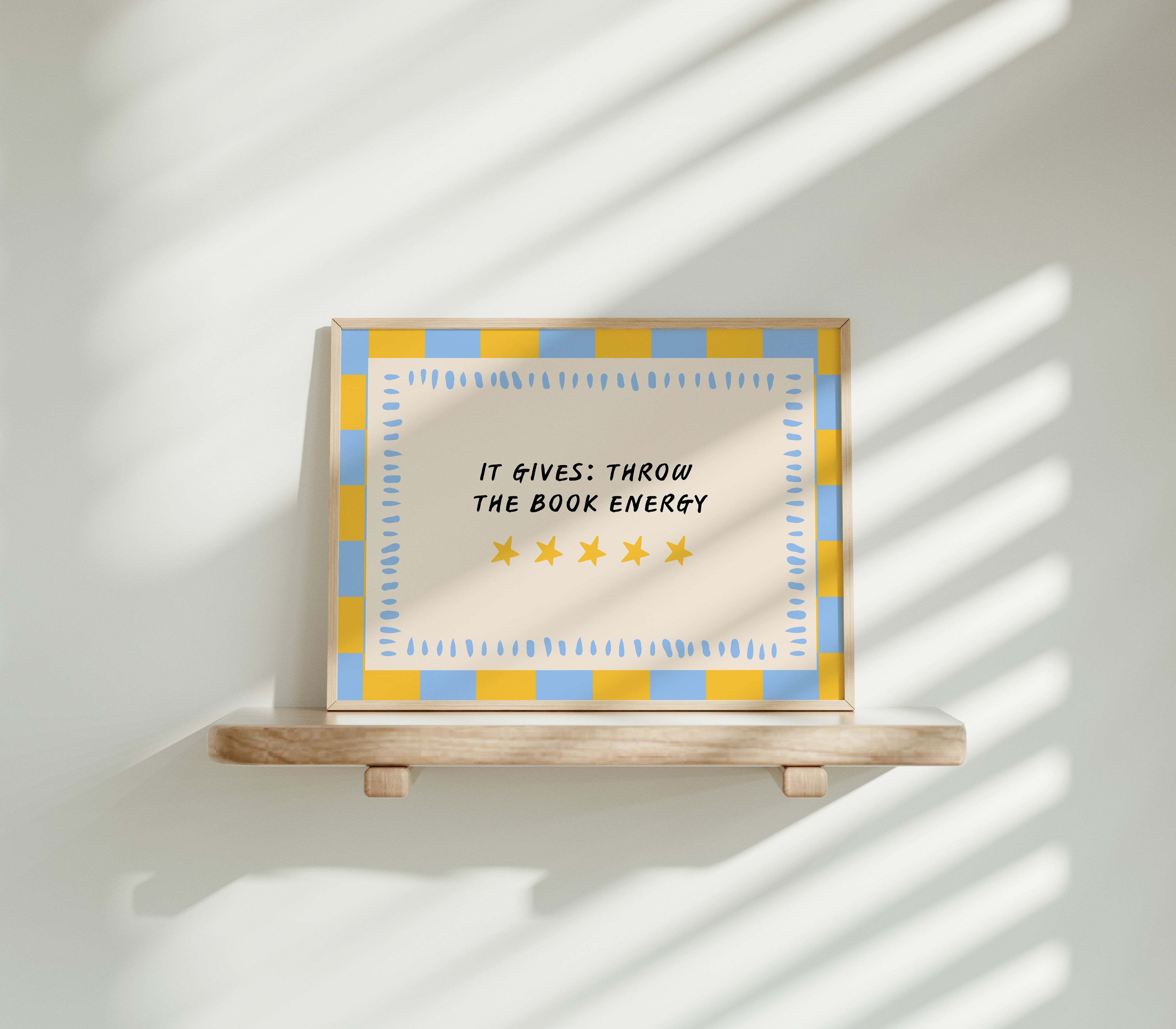 It Gives: Throw the Book Energy horizontal 24x36 bookish wall art poster displayed on a wooden shelf against a sunlit white wall